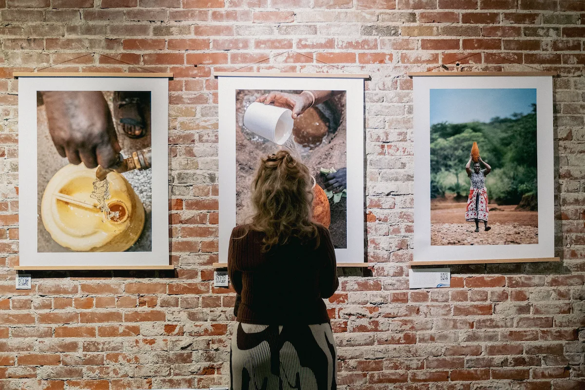 Large-format photo prints from a Water Mission exhibit, printed by RB Printing, hanging on a brick gallery wall